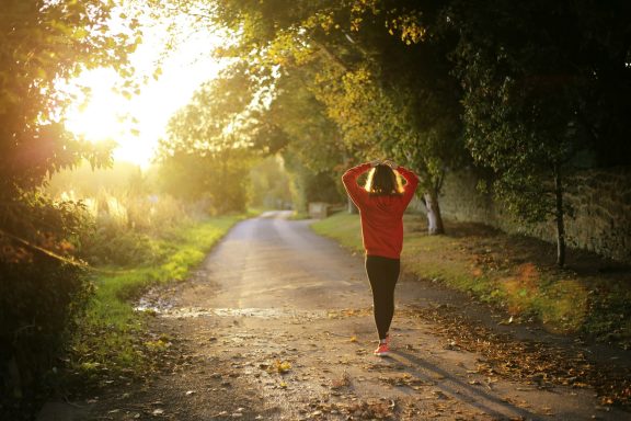Eine Person in roter Jacke joggt auf einem von Bäumen gesäumten Weg bei Sonnenuntergang.